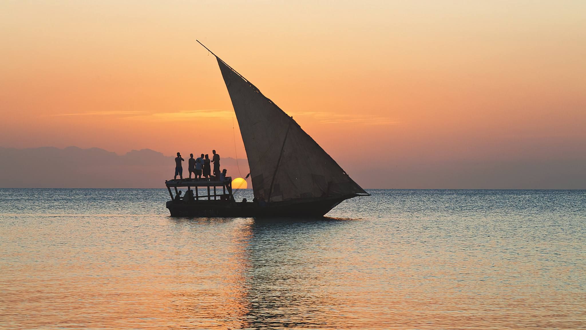 A traditional dhow sailing on the Indian Ocean off the Kenya coast, with a palm-fringed shore behind